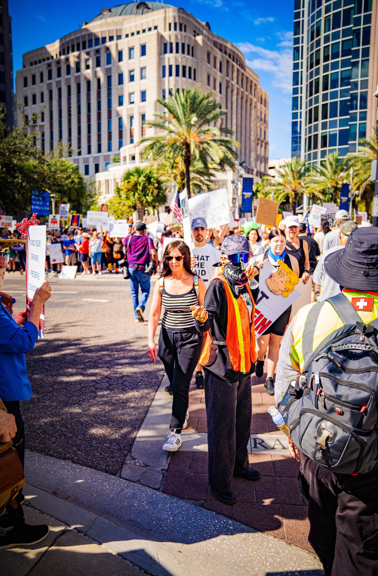 Protesters gathering outside a modern office building with palm trees under bright blue skies.
