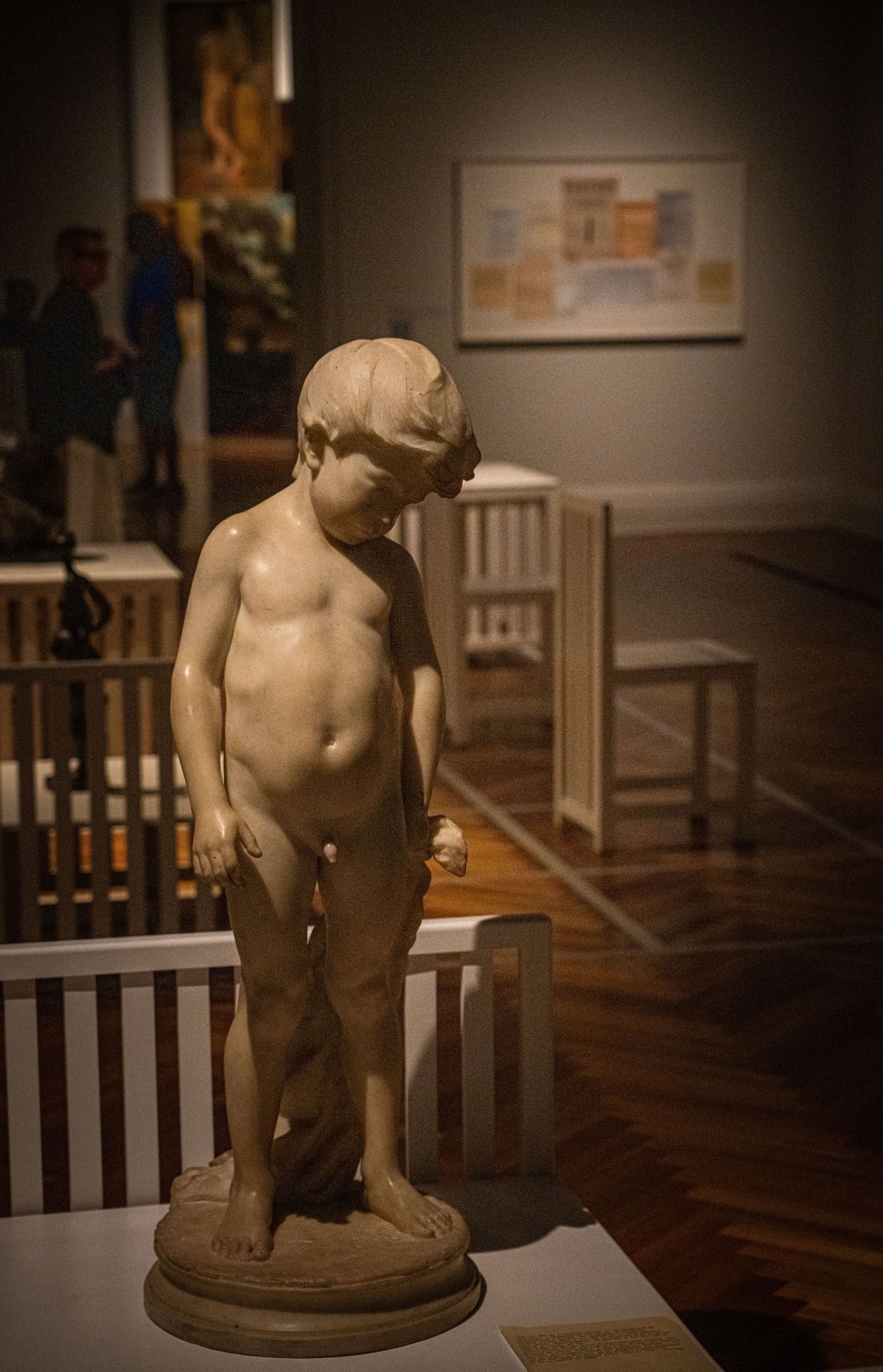 Classical marble sculpture of a young child figure displayed on a pedestal in a museum.