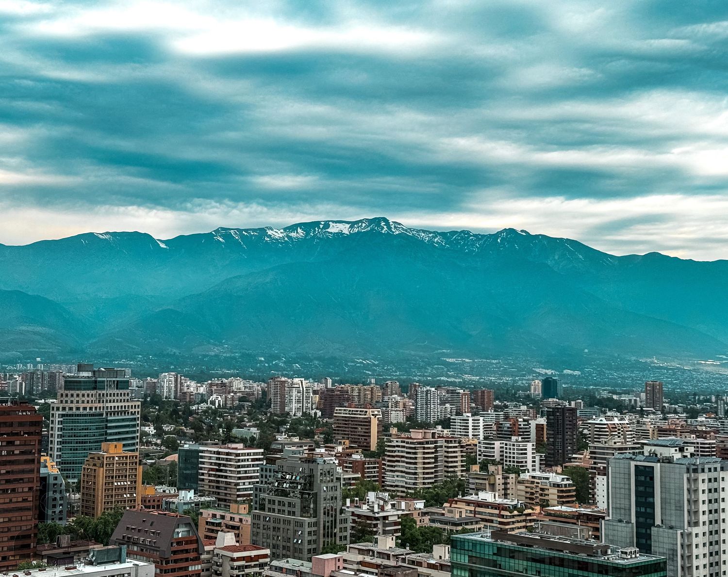 Panoramic cityscape view of Santiago Chile with snow-capped Andes mountains in the background.
