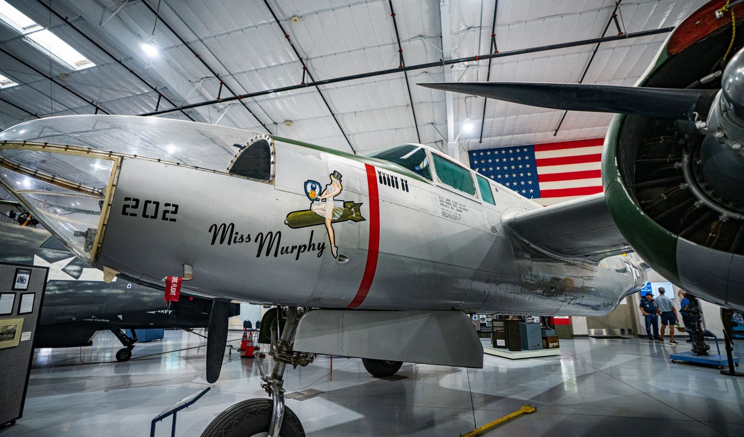 Vintage WWII-era Miss Murphy military aircraft on display in an aviation museum hangar with American flag backdrop.