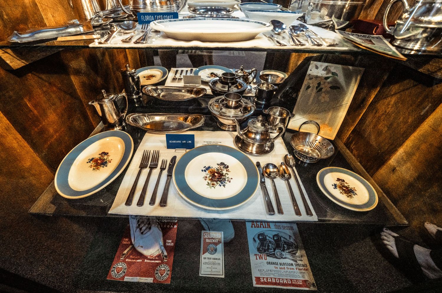 Multiple formal place settings arranged on wooden tables with elegant dinnerware and glassware.