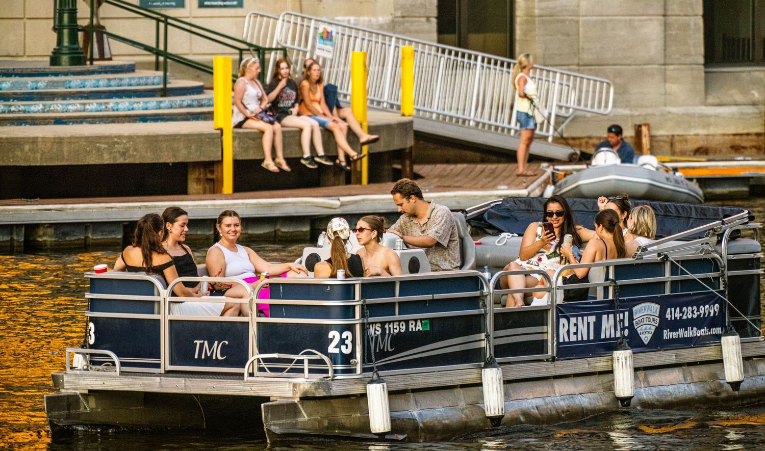 Waterfront scene showing several rental boats with people relaxing and socializing.