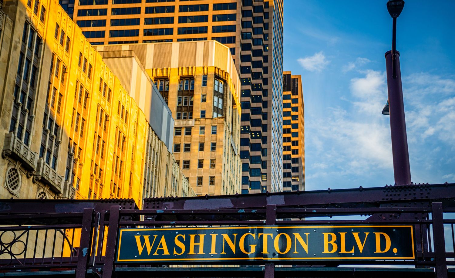 Street sign for Washington Boulevard in downtown Chicago with golden sunlit buildings in background.