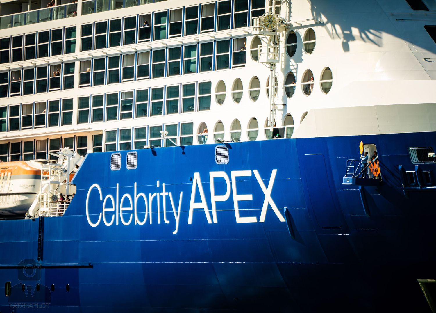 Cruise ship exterior with Celebrity APEX logo and signage illuminated against a dark blue background.