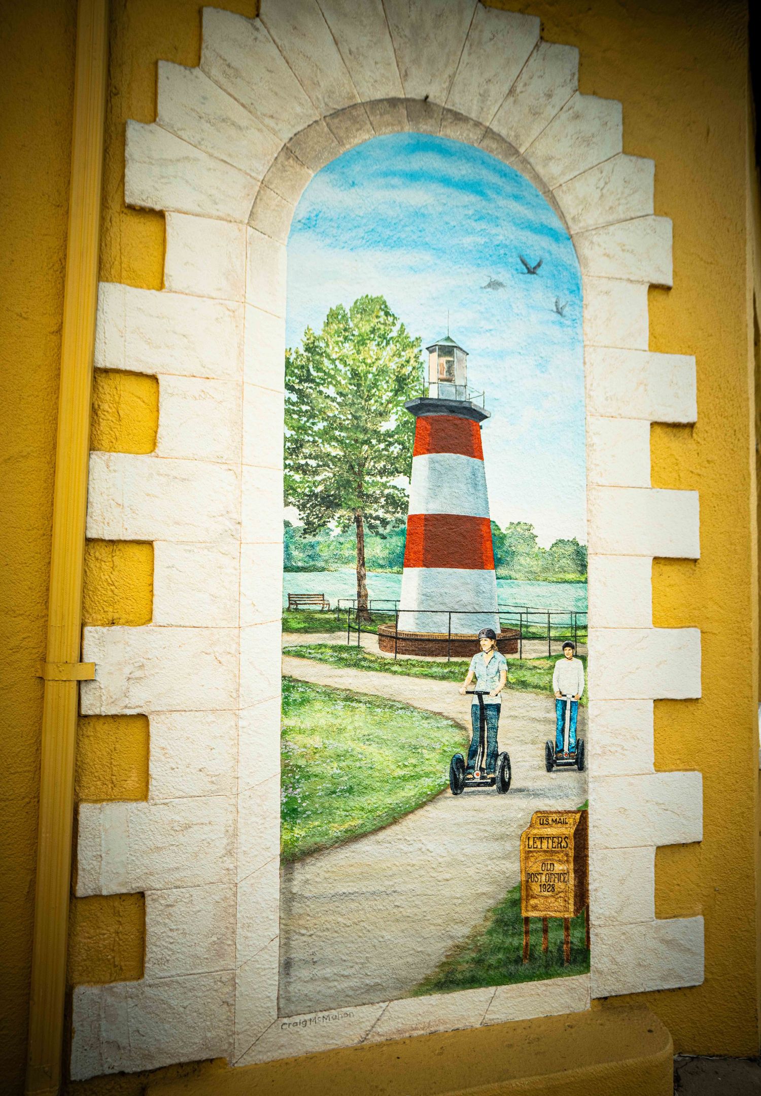 A series of arched stone doorways with yellow accents frame a painted mural depicting a lighthouse and coastal scene.