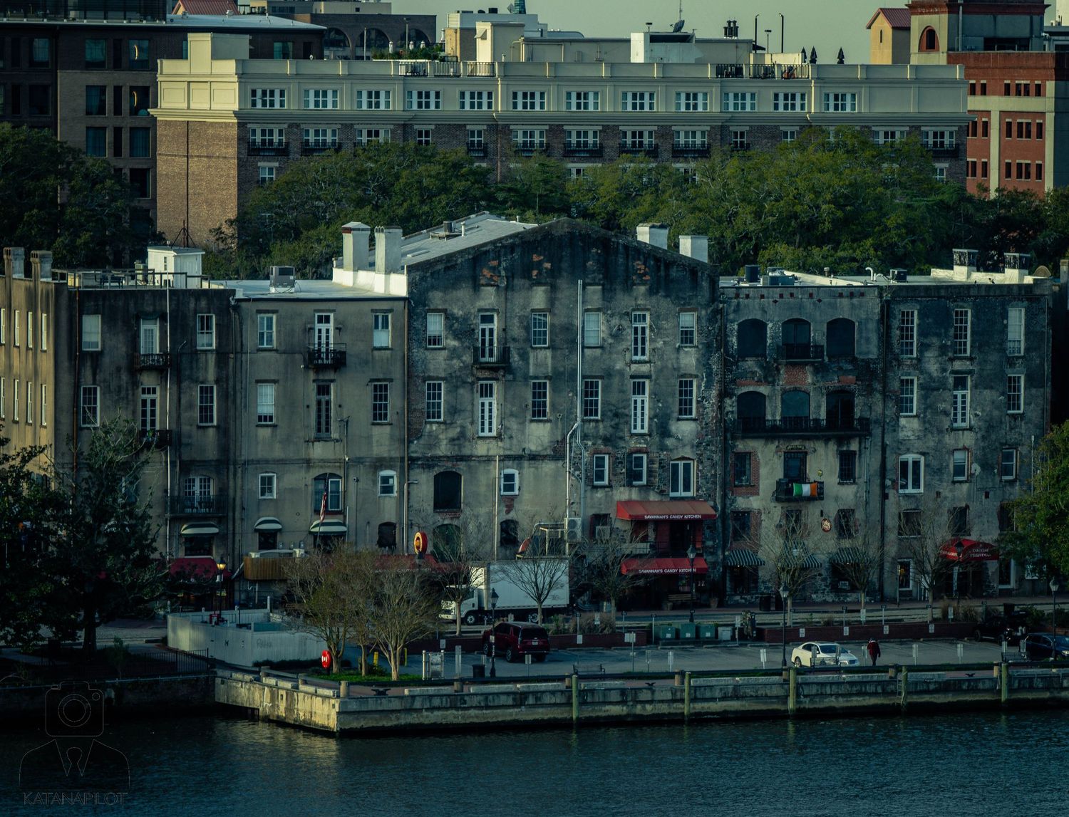 A panoramic cityscape view shows historic stone buildings along a waterfront with boats docked at the pier.