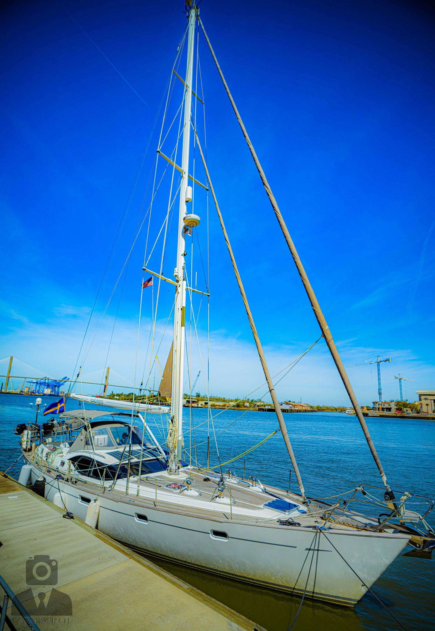 Panoramic view of white sailboat moored at dock against vibrant blue sky on calm waters.