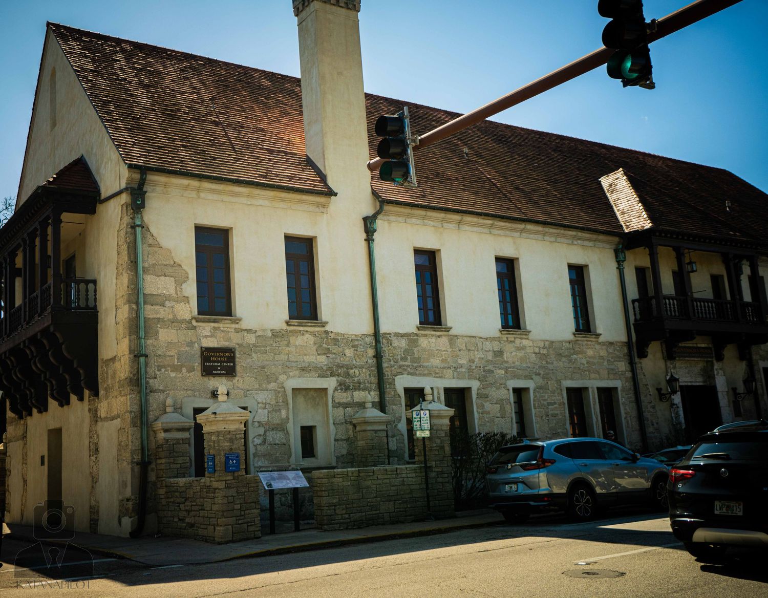 Historic row of white colonial buildings with tiled roofs and parked cars along a sunny street in St. Augustine.
