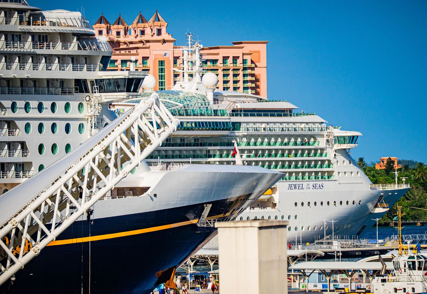 Large white cruise ship Jewel of the Seas docked at a tropical port with colorful resort buildings in the background.