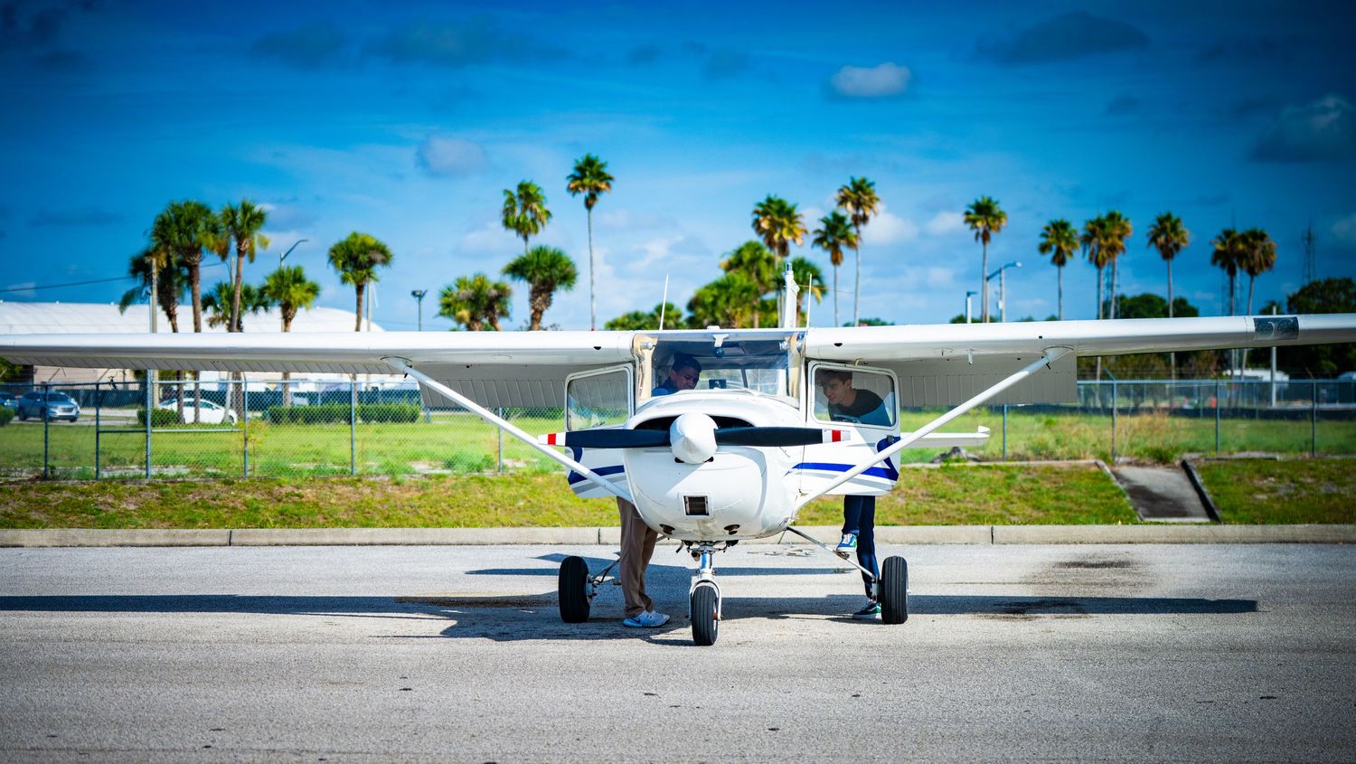 Small private planes parked on airfield with tropical palm trees in distance.
