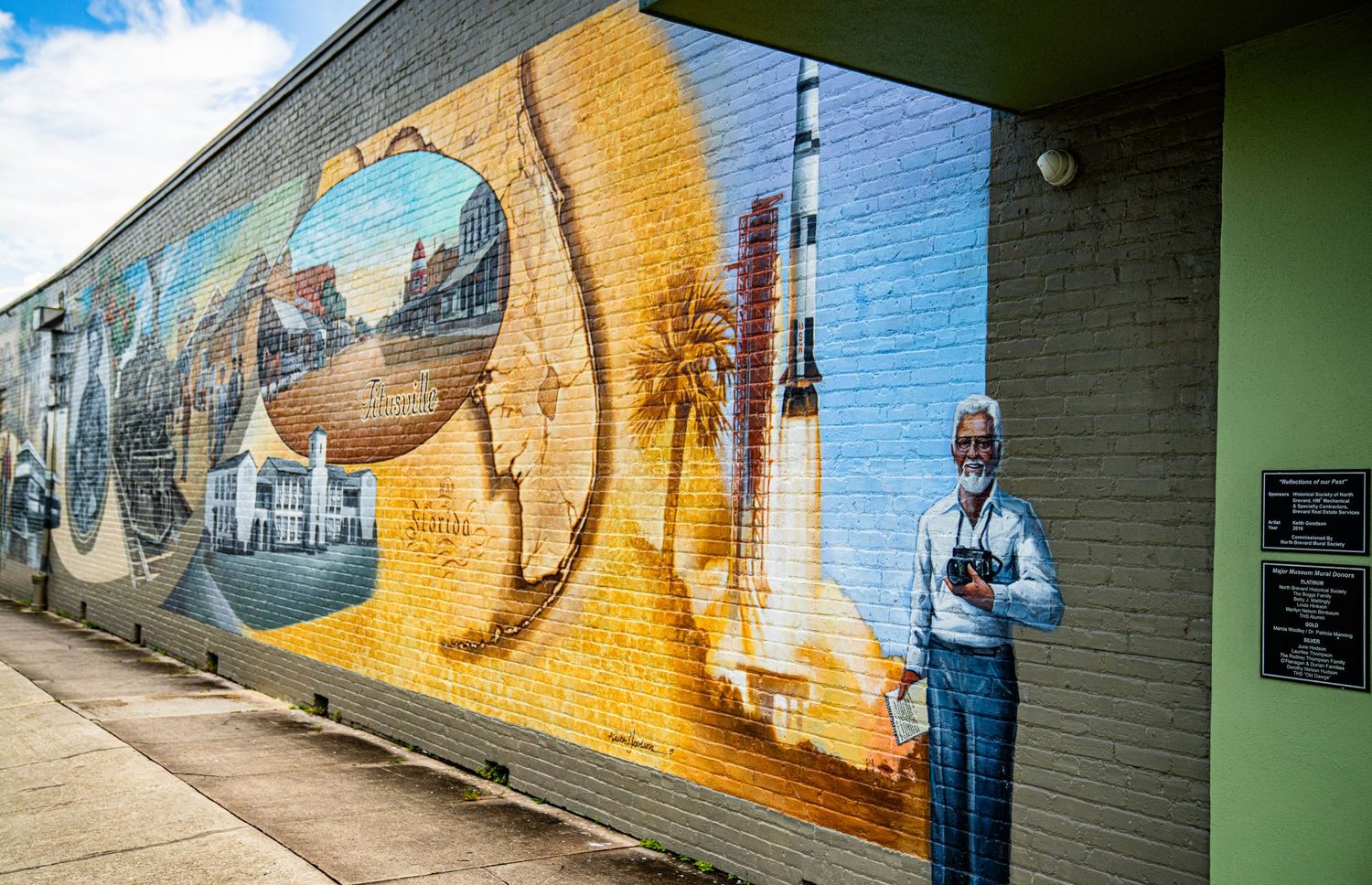 Large outdoor mural depicting space and coastal themes on brick wall.
