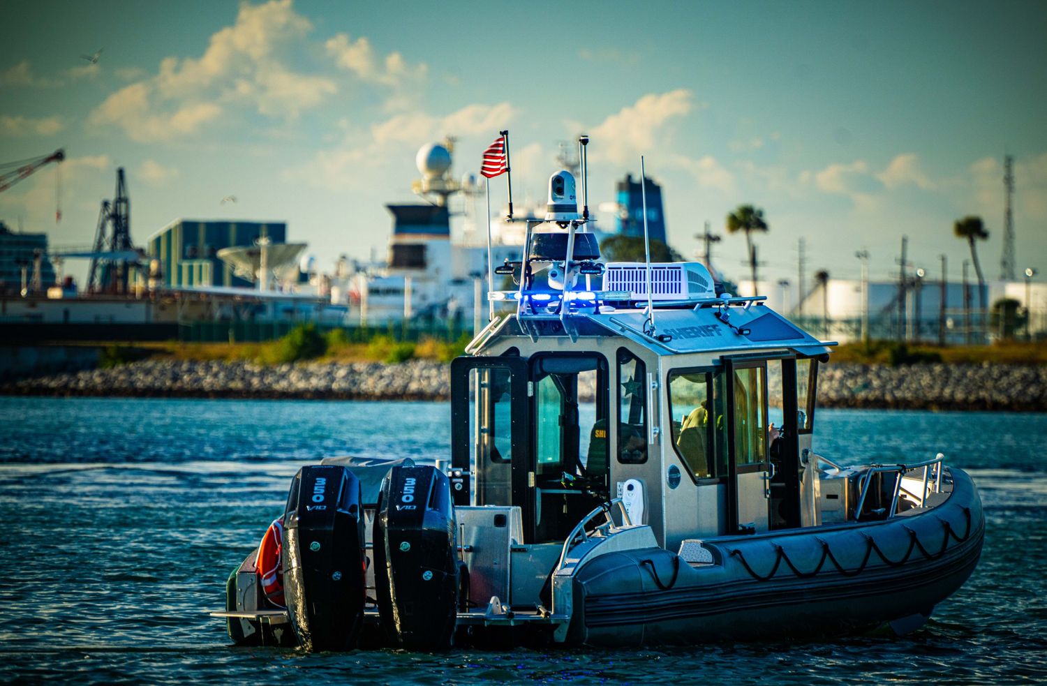 A row of fishing boats docked at a marina with palm trees and blue skies in the background.