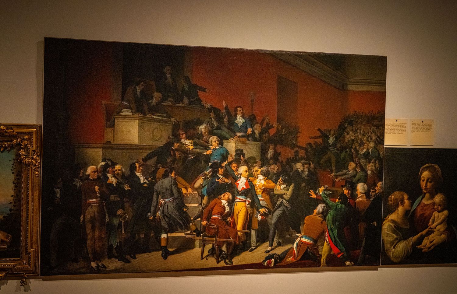 Large classical painting showing a crowded historical scene with dramatic lighting.