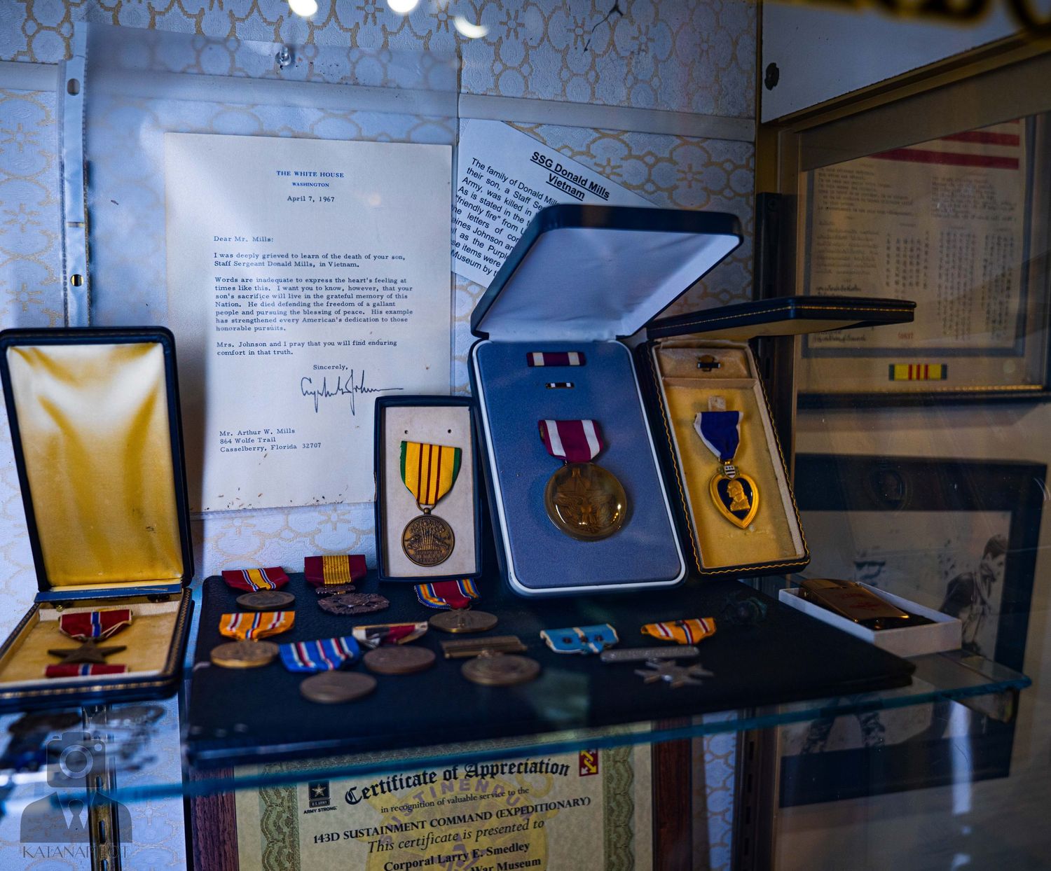 Display case showing various military medals, awards and certificates in presentation boxes.