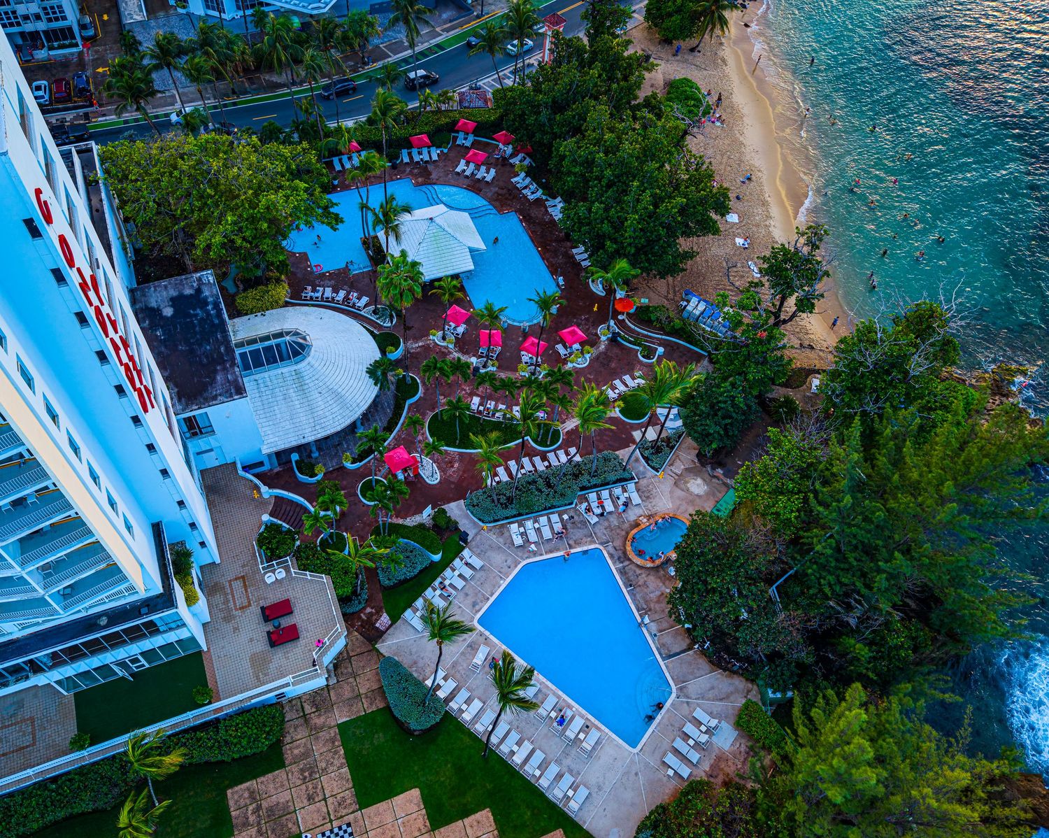 Bird's eye view of luxury beachfront resort with swimming pools and landscaped grounds along tropical coastline.