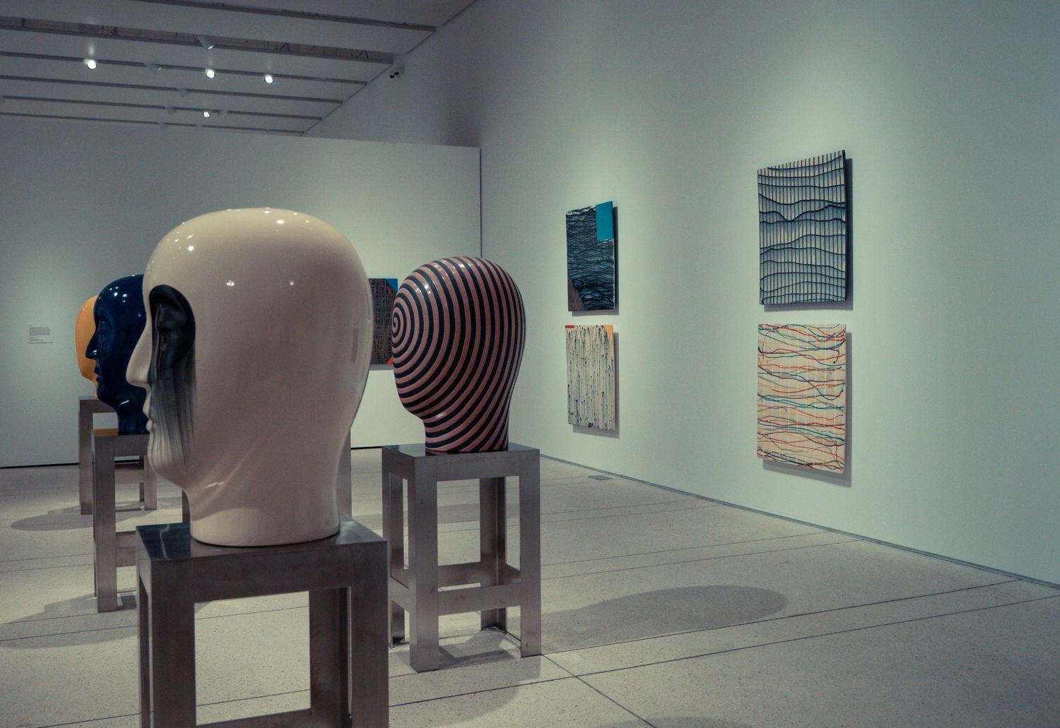 A panoramic view of a modern art gallery interior with white walls displaying abstract artworks and sculptures.