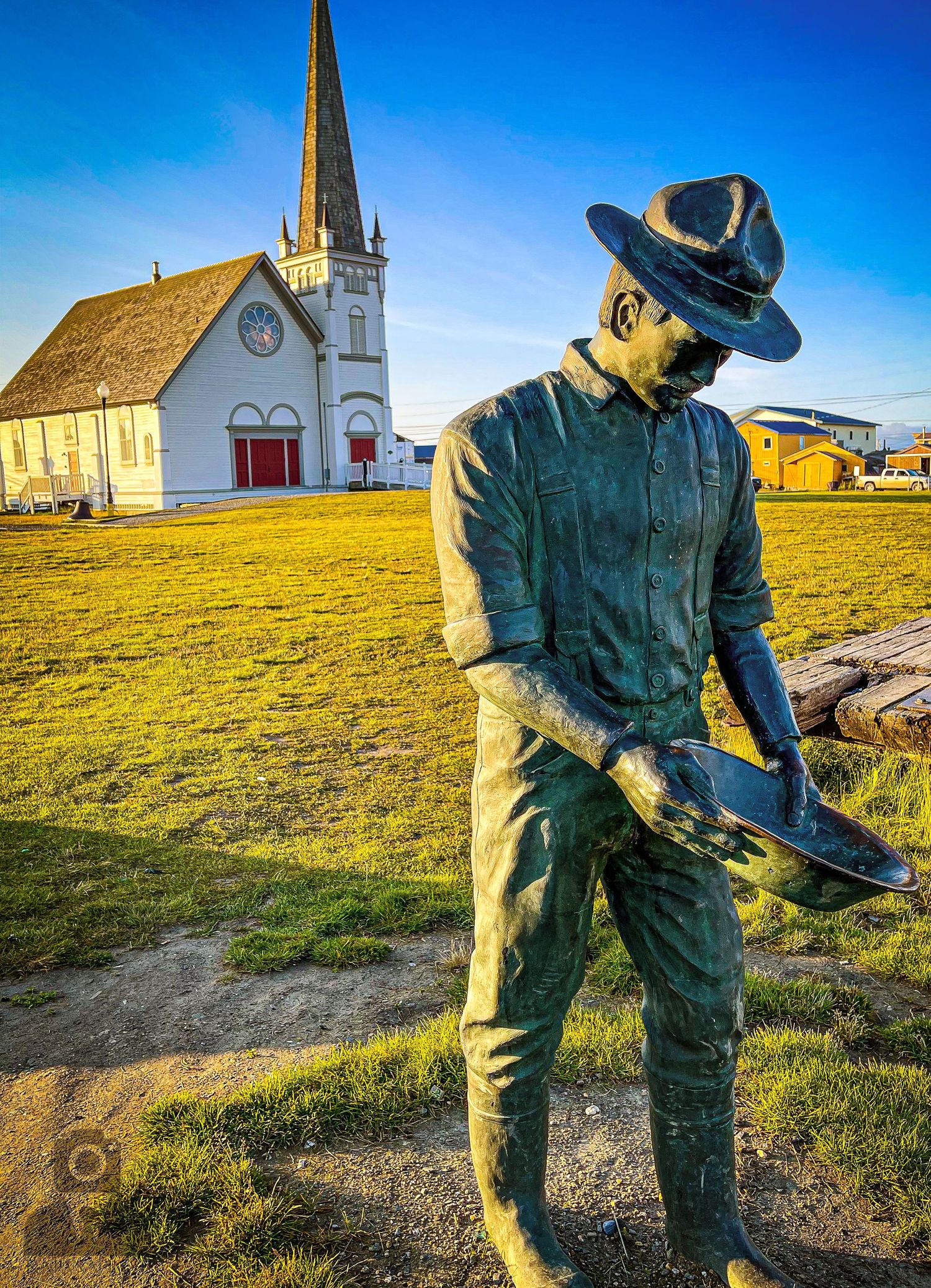 Bronze statues of gold miners stand near a white church building in Nome, Alaska.