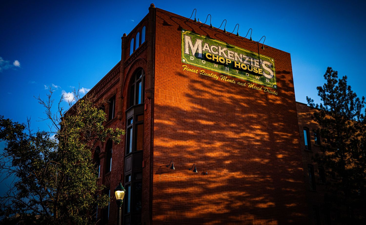 Mackenzie's Chop House brick building exterior at dusk with dramatic blue sky and tree shadows.
