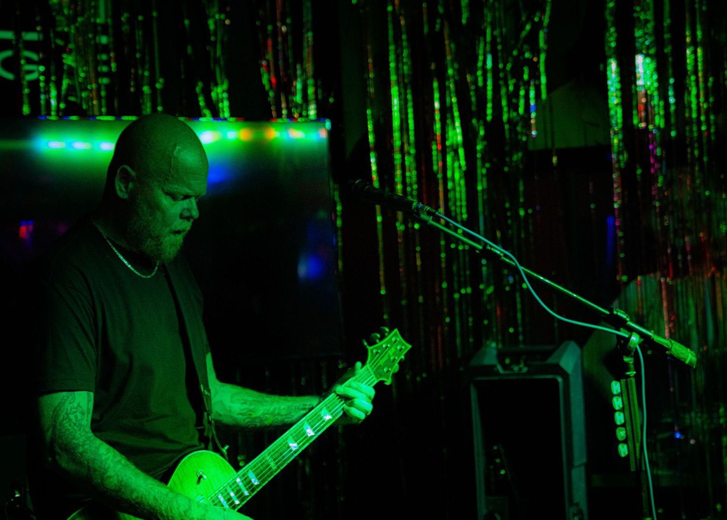 Guitarist performing on stage illuminated by green stage lighting during a rock concert.