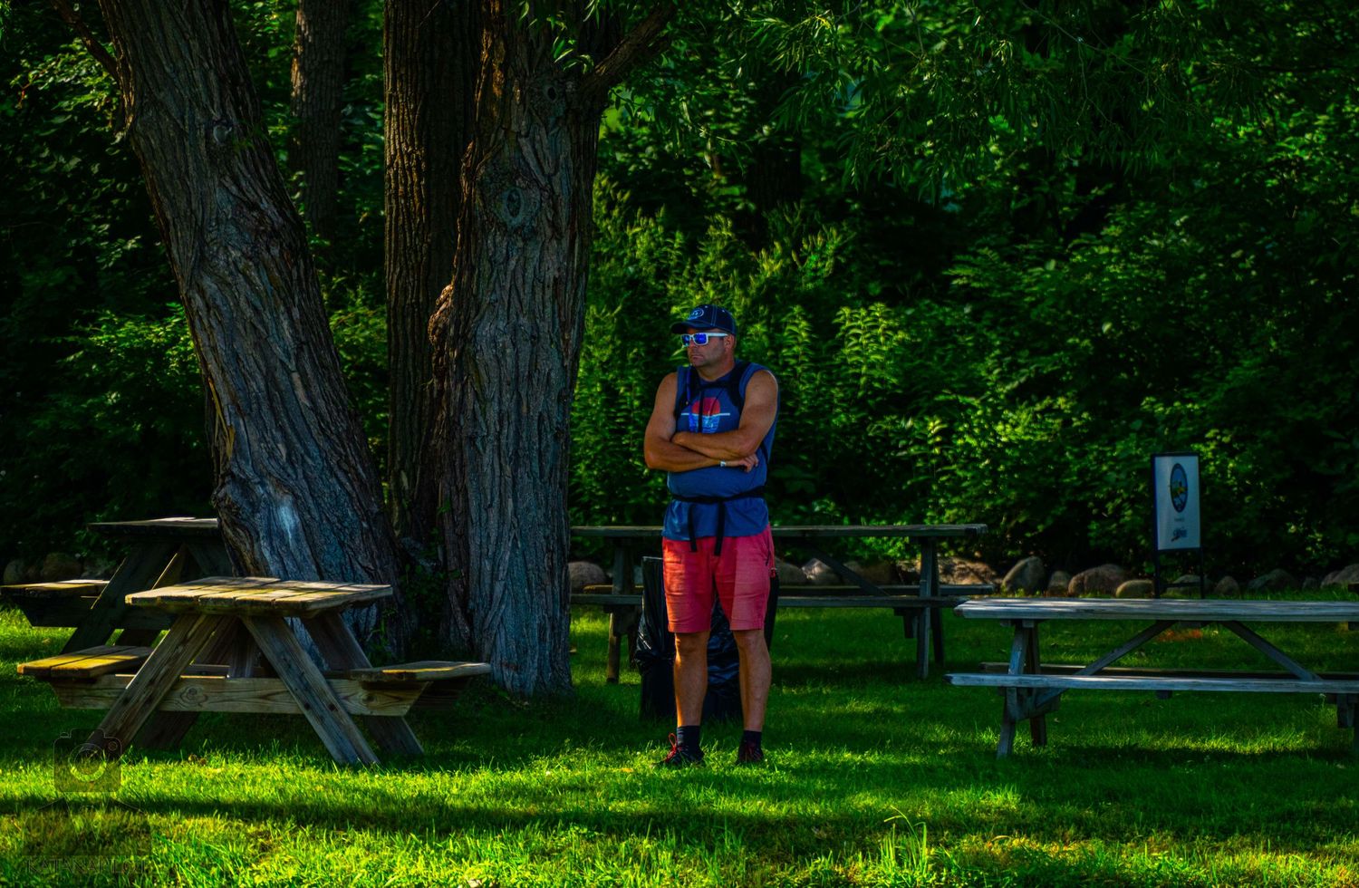 Person relaxing at a shaded picnic area surrounded by tall trees in a peaceful park setting.