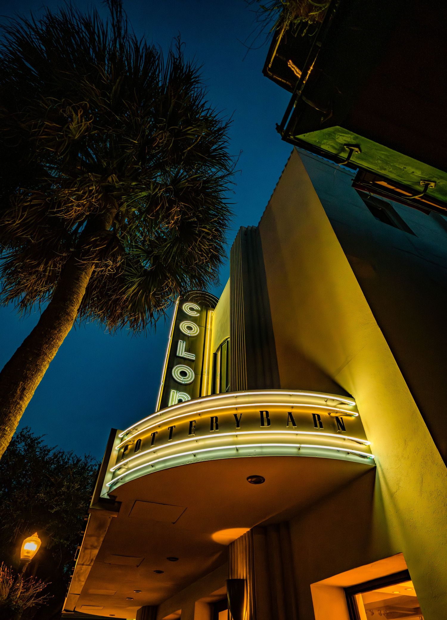 Art deco style building facade illuminated at night with palm trees silhouetted against dark sky.