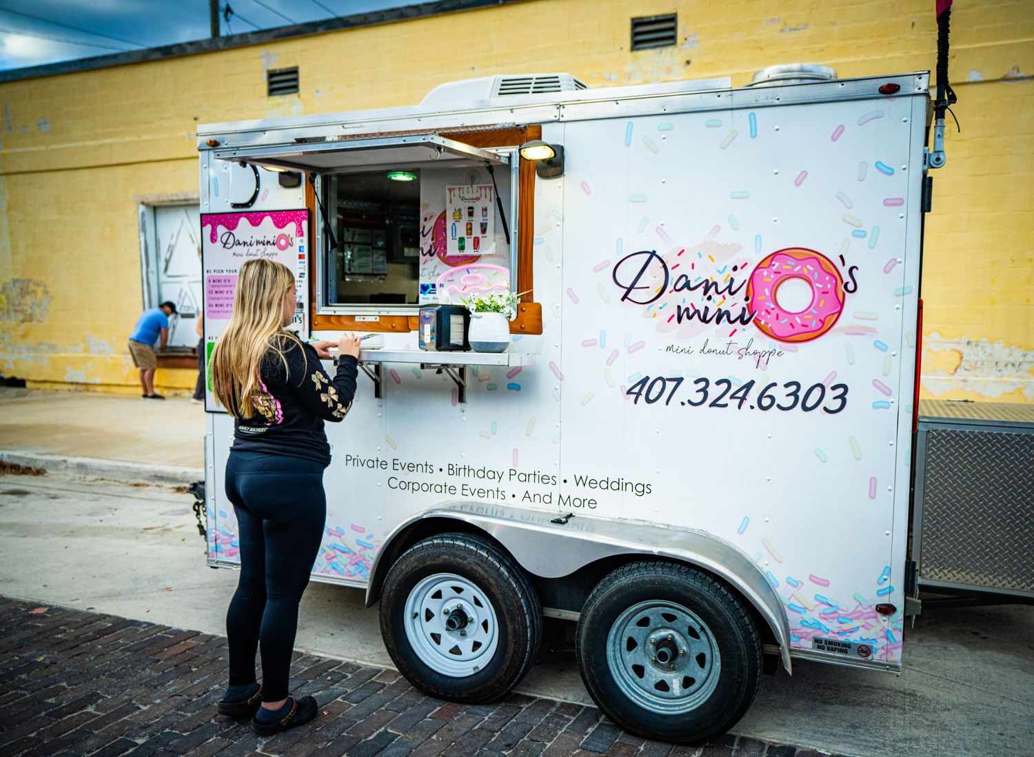 A mobile donut food truck with pink and white branding parked on a street.