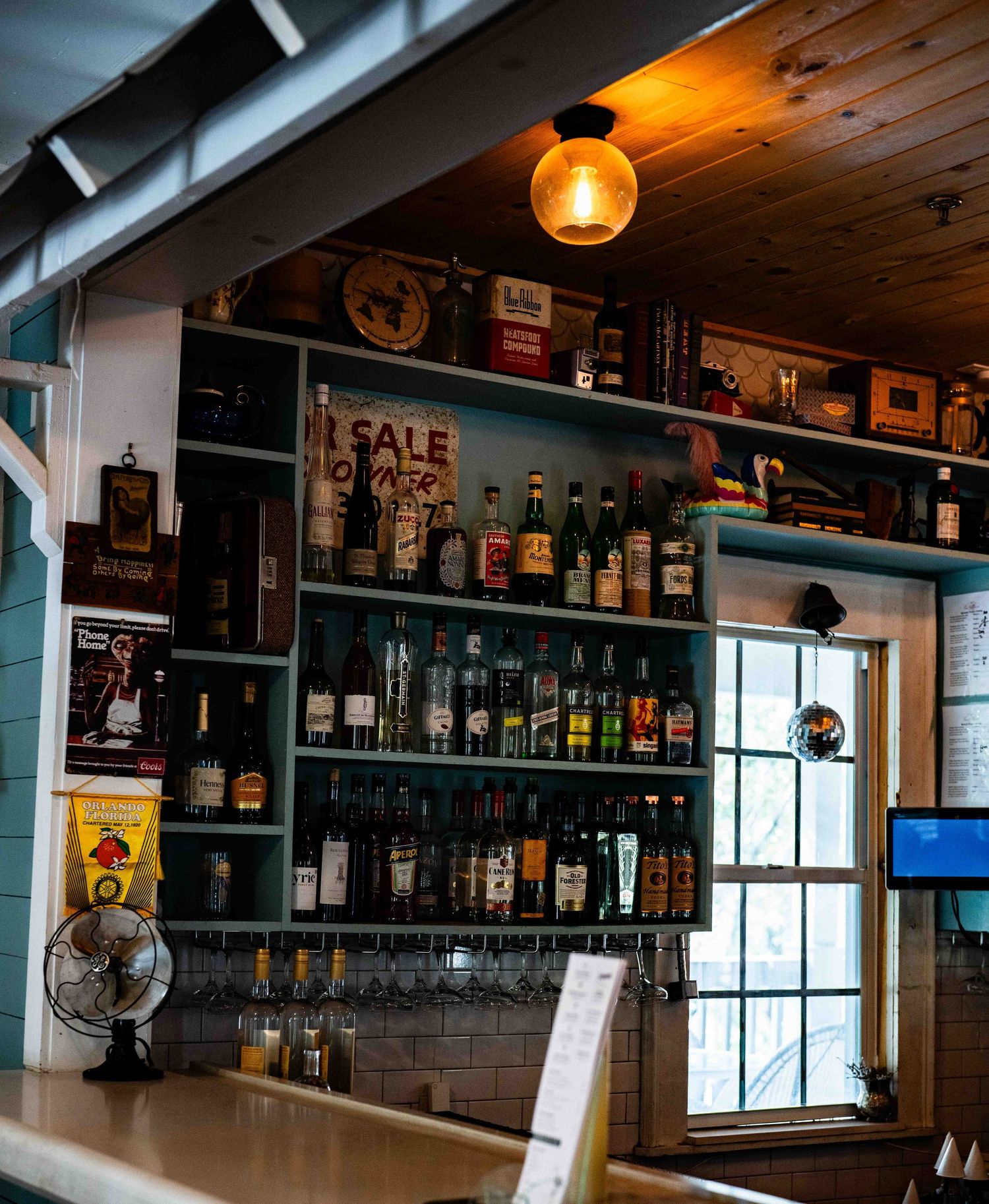 A rustic bar interior with wooden shelves displaying various liquor bottles and warm pendant lighting.