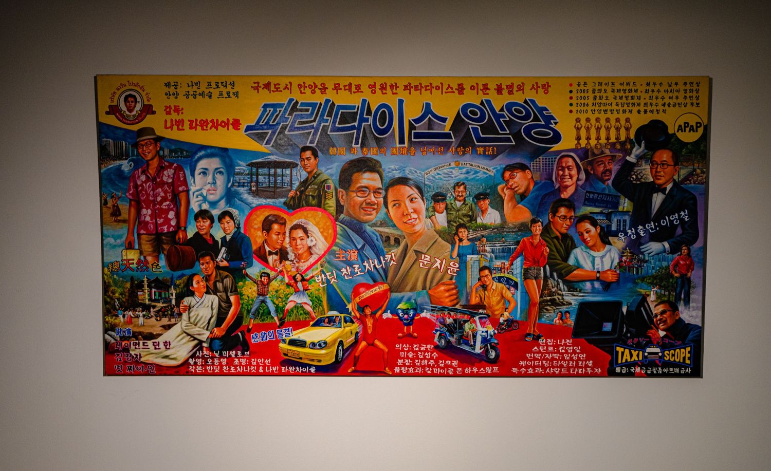 Colorful Korean movie poster displayed on a white wall featuring vibrant illustrated characters and bold text.