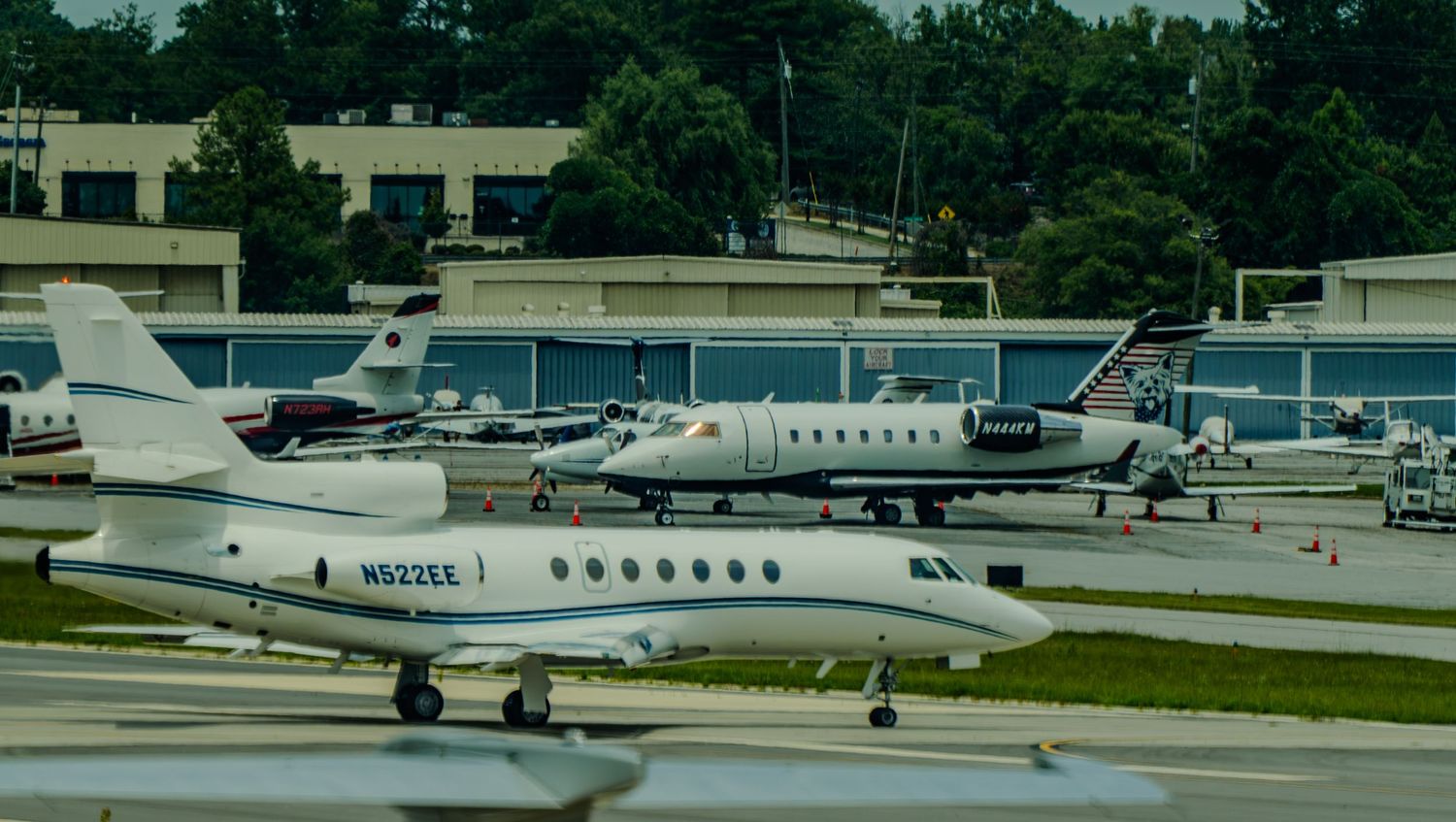 Multiple private jets parked on tarmac at a busy general aviation airport surrounded by lush green trees.