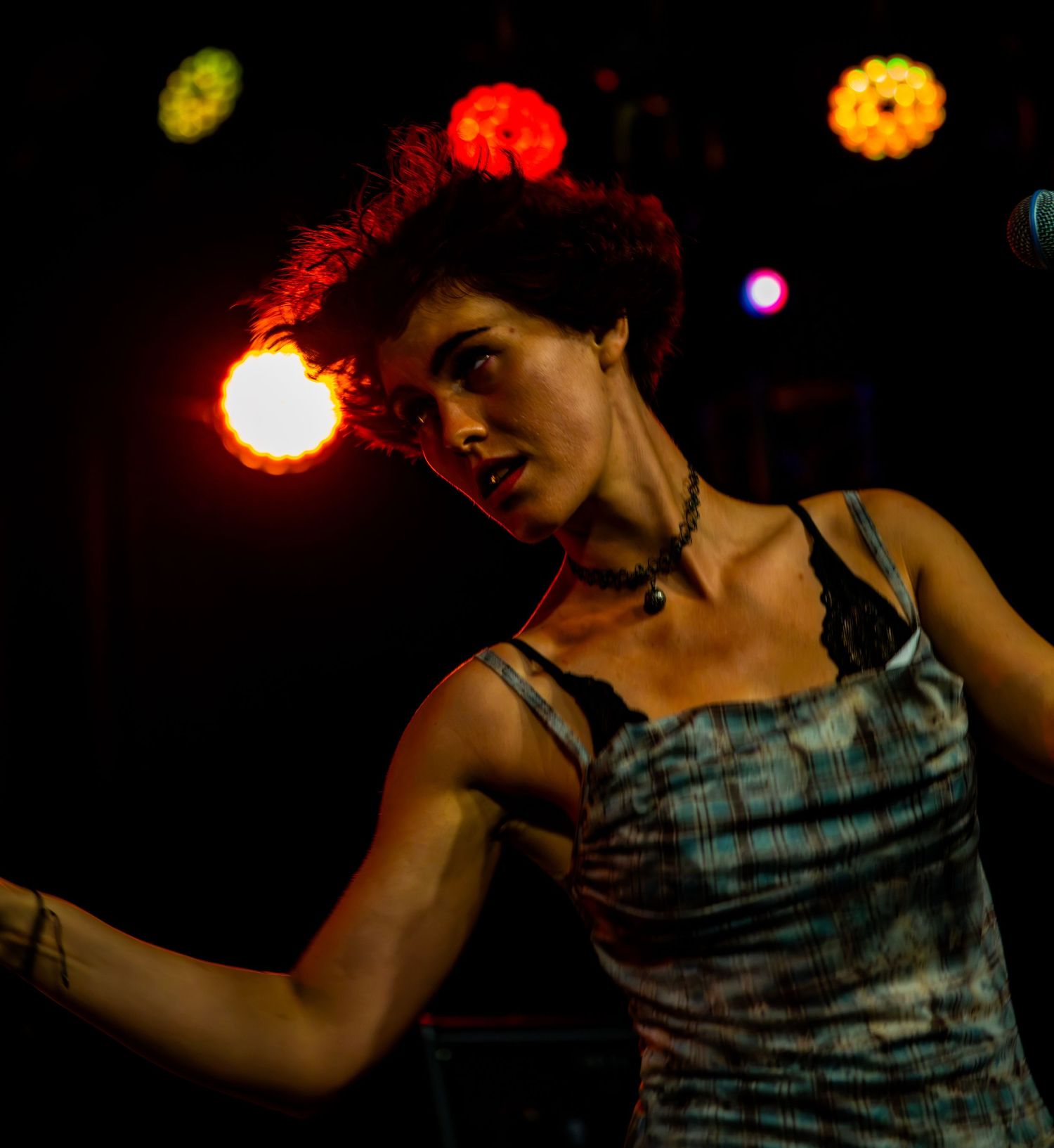 Female performer with red hair dancing under warm stage lighting wearing a plaid top.