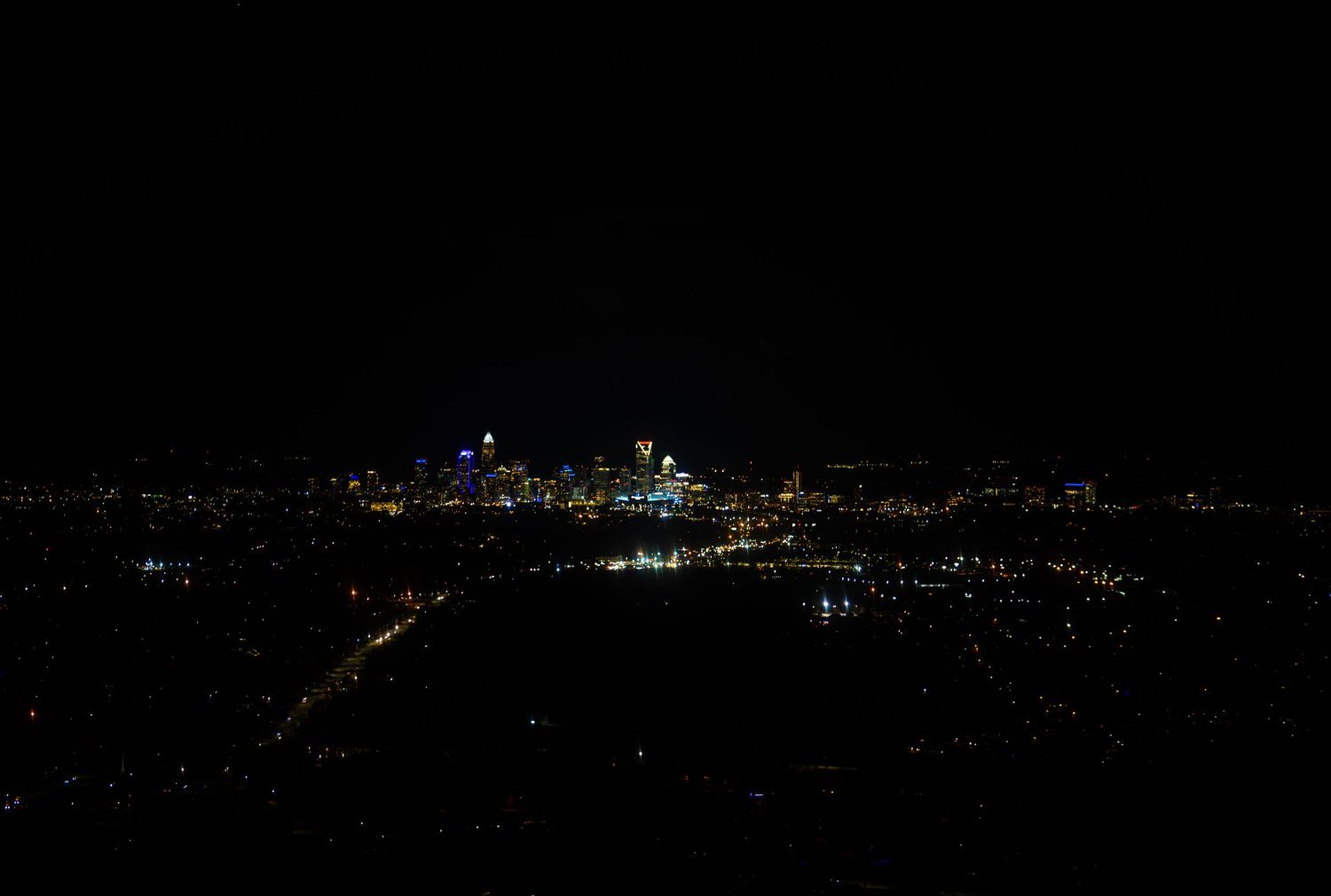 Panoramic night view of city lights stretching across a dark horizon with illuminated buildings and streets.