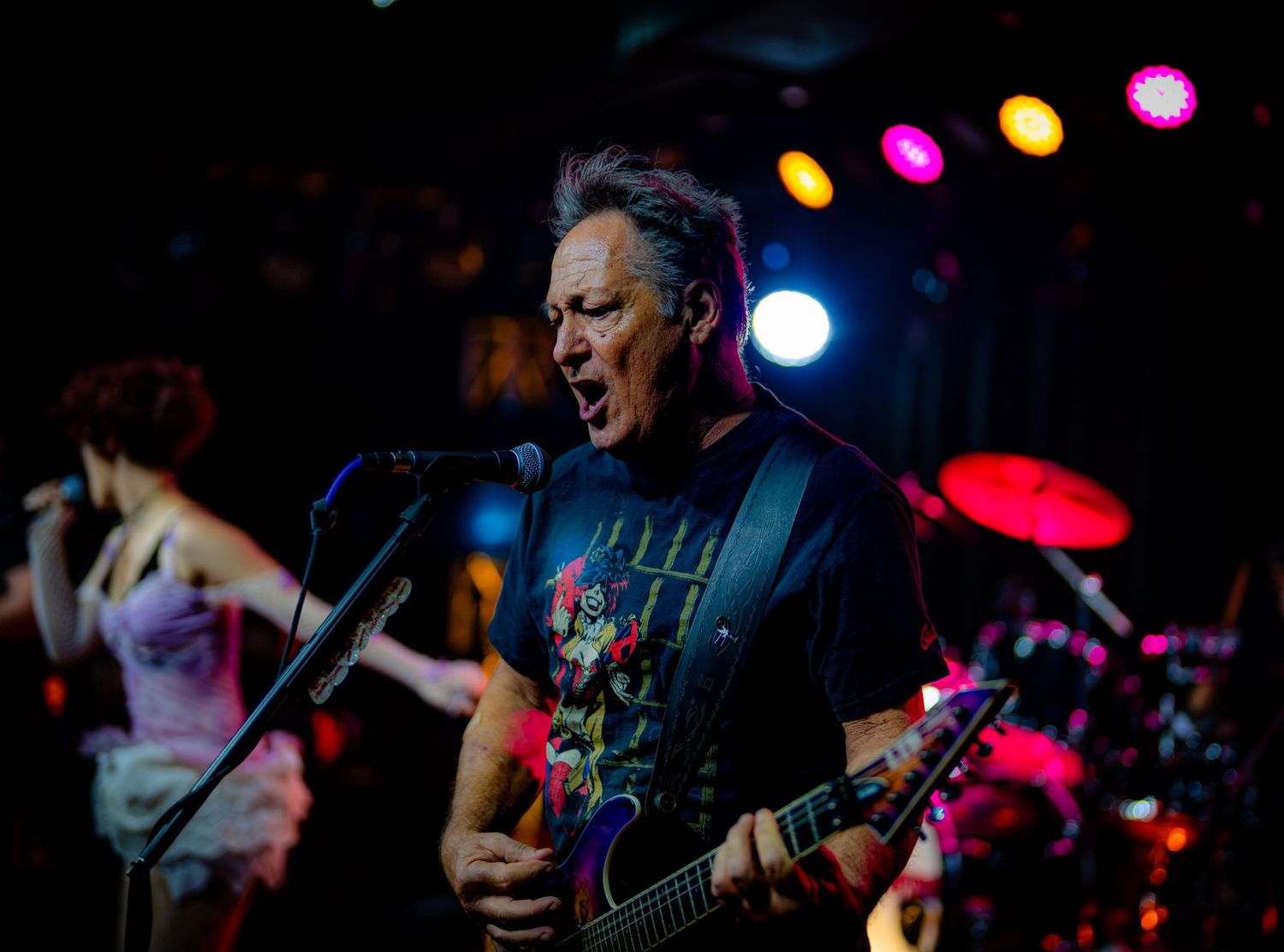 Male guitarist singing passionately on stage under colorful lights at a live rock concert.
