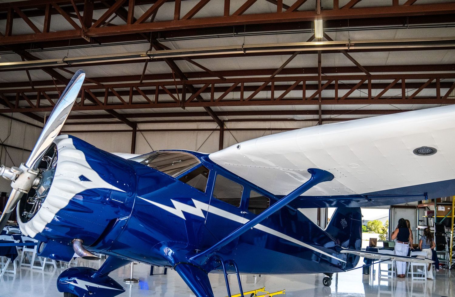 Aviation hangar interior showing multiple aircraft under exposed beam ceiling.