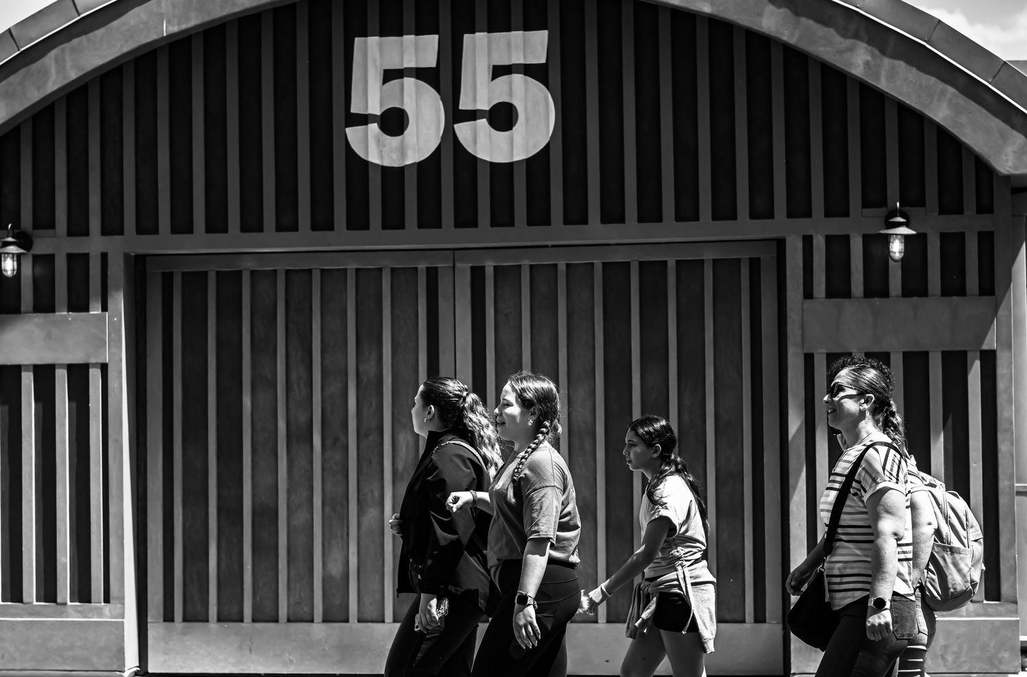 A black and white panoramic photograph shows a row of numbered horse stables with striped awnings at a racetrack.