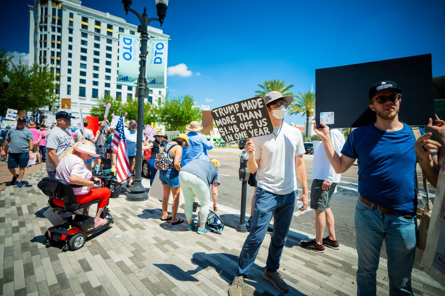 A crowd of people gathered on a sidewalk in an urban area during a sunny day.