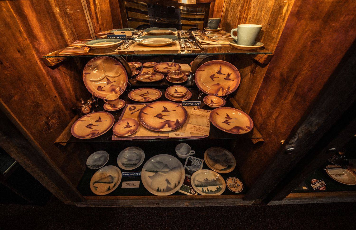 Collection of vintage railroad plates and dinnerware displayed in wooden museum cases.
