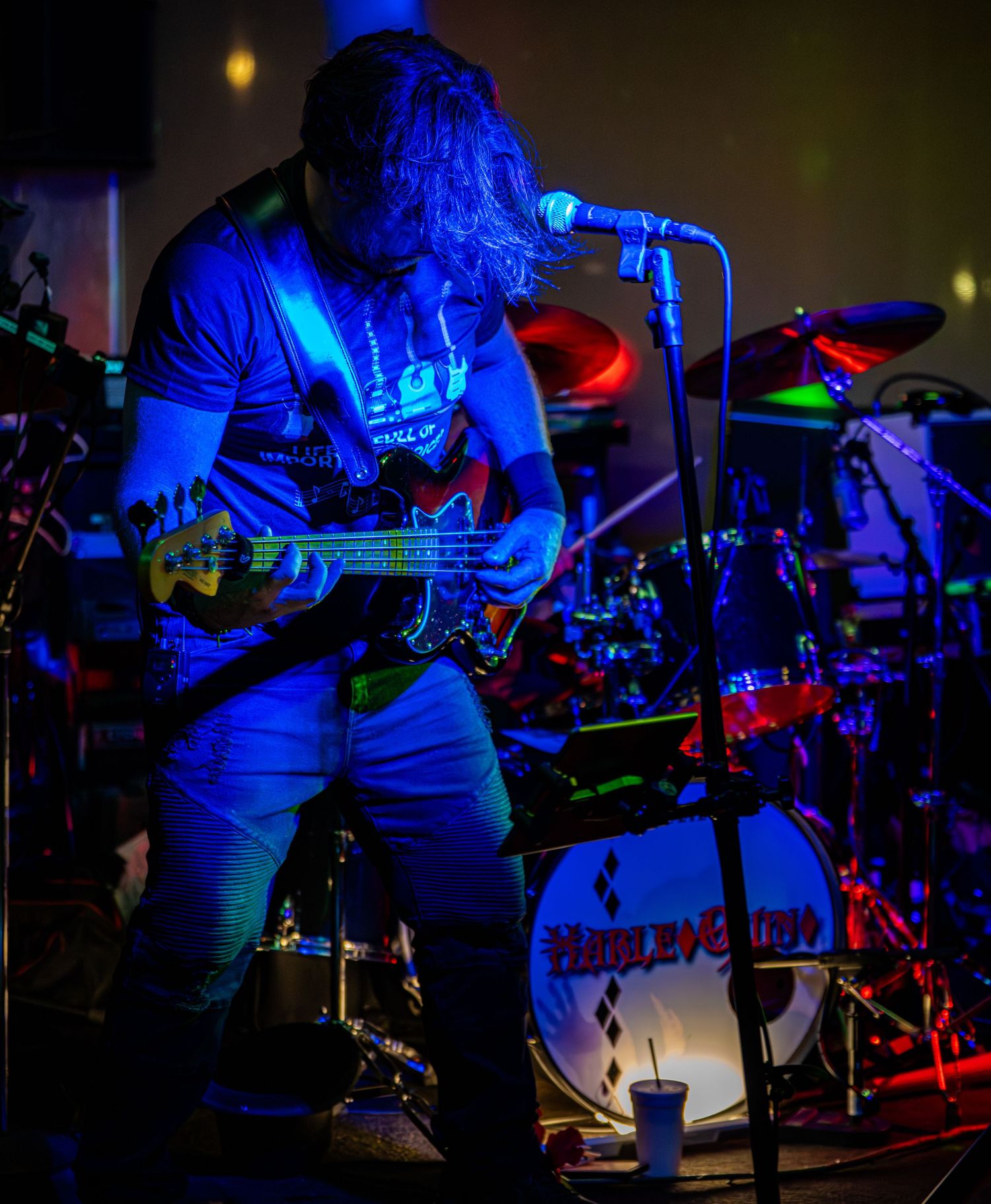 Band performing on stage with drum kit visible under blue concert lighting.