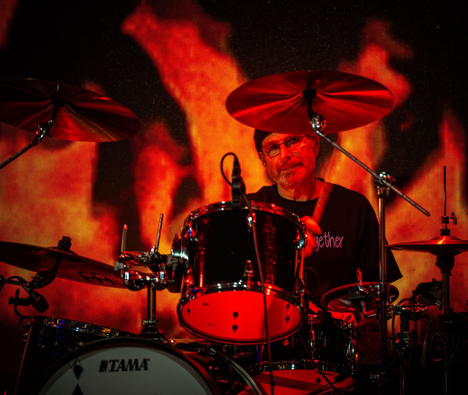 Drum kit illuminated by intense red stage lighting during a live performance.