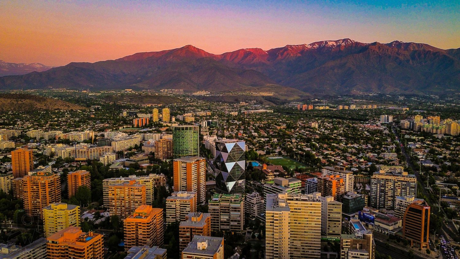 Panoramic cityscape view with mountains and colorful sunset sky.