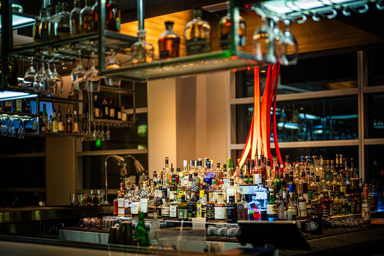Illuminated upscale bar counter with rows of liquor bottles and glowing ambient lighting.