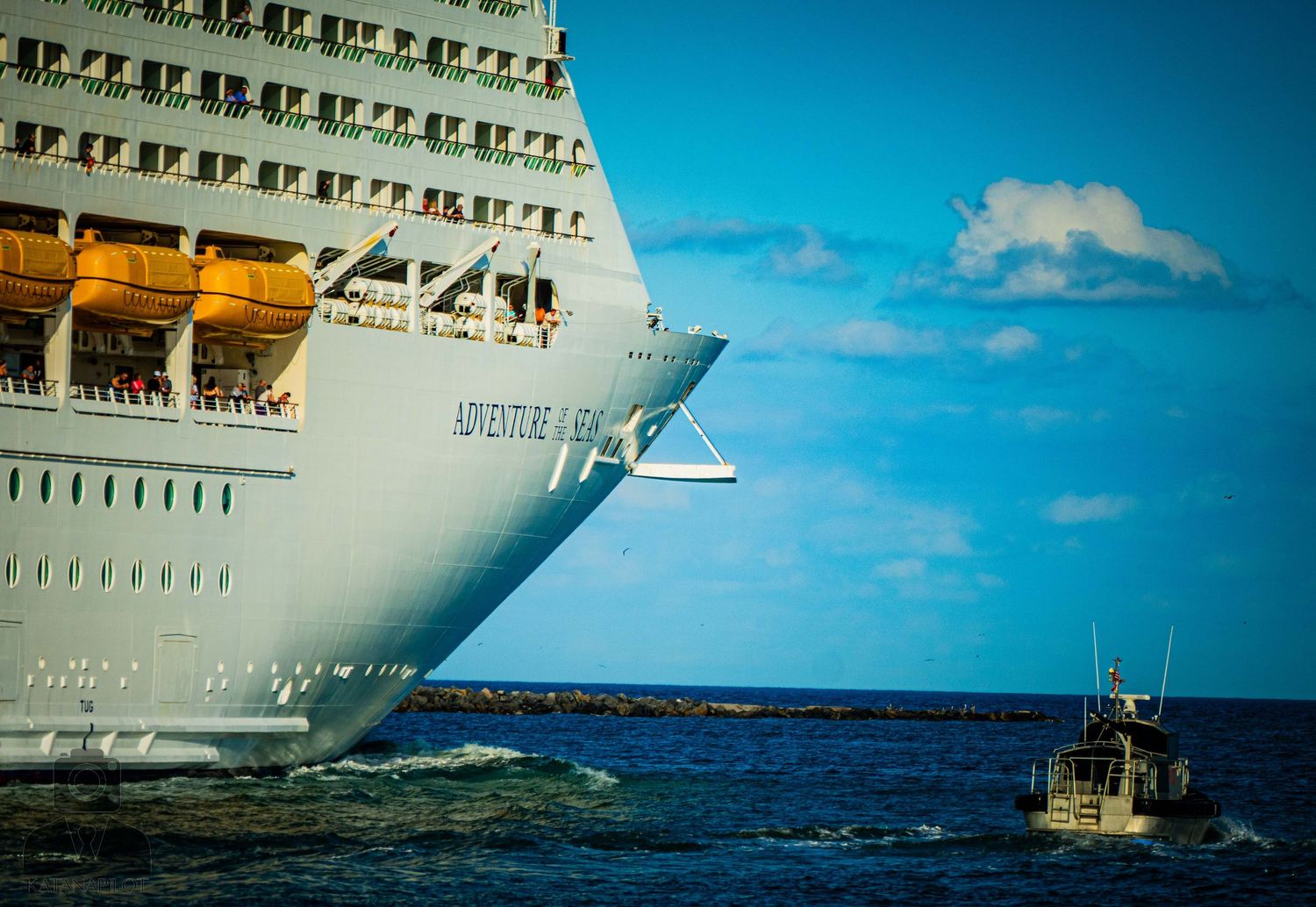 Large white cruise ship hull against bright blue sky and ocean on a sunny day.