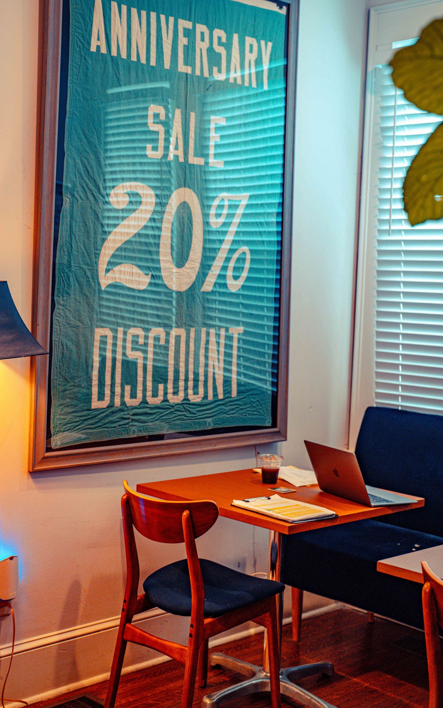 Restaurant interior with blue anniversary sale posters advertising 20% discount on white walls above wooden tables and chairs.