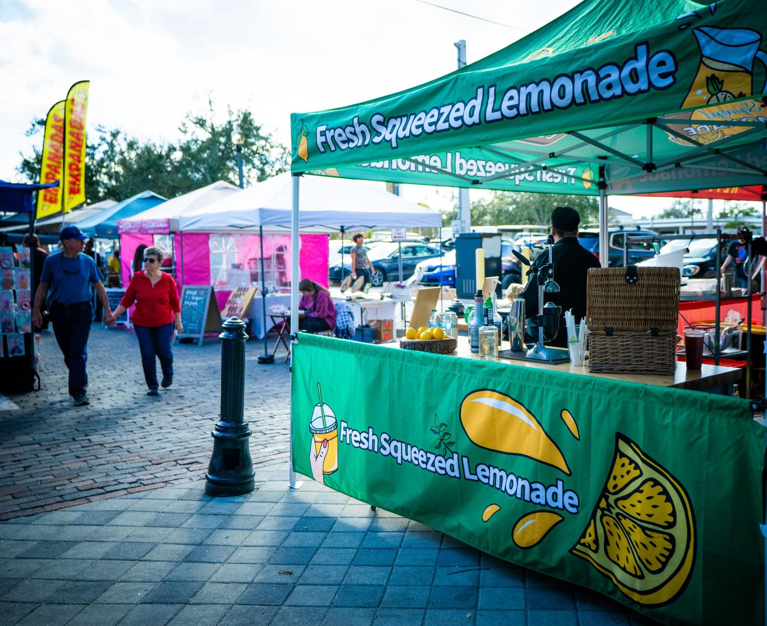Green vendor tents with Fresh Squeezed Lemonade signage line a street market on a cloudy day.