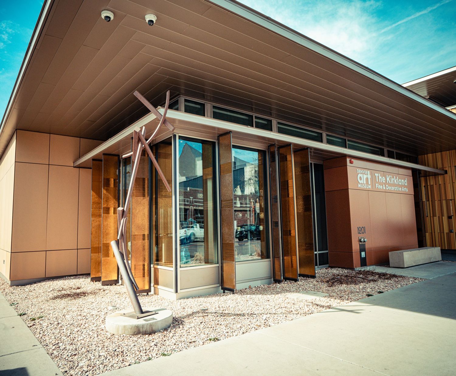 Modern commercial building entrance with copper-colored exterior panels and glass doors under an extended overhang.