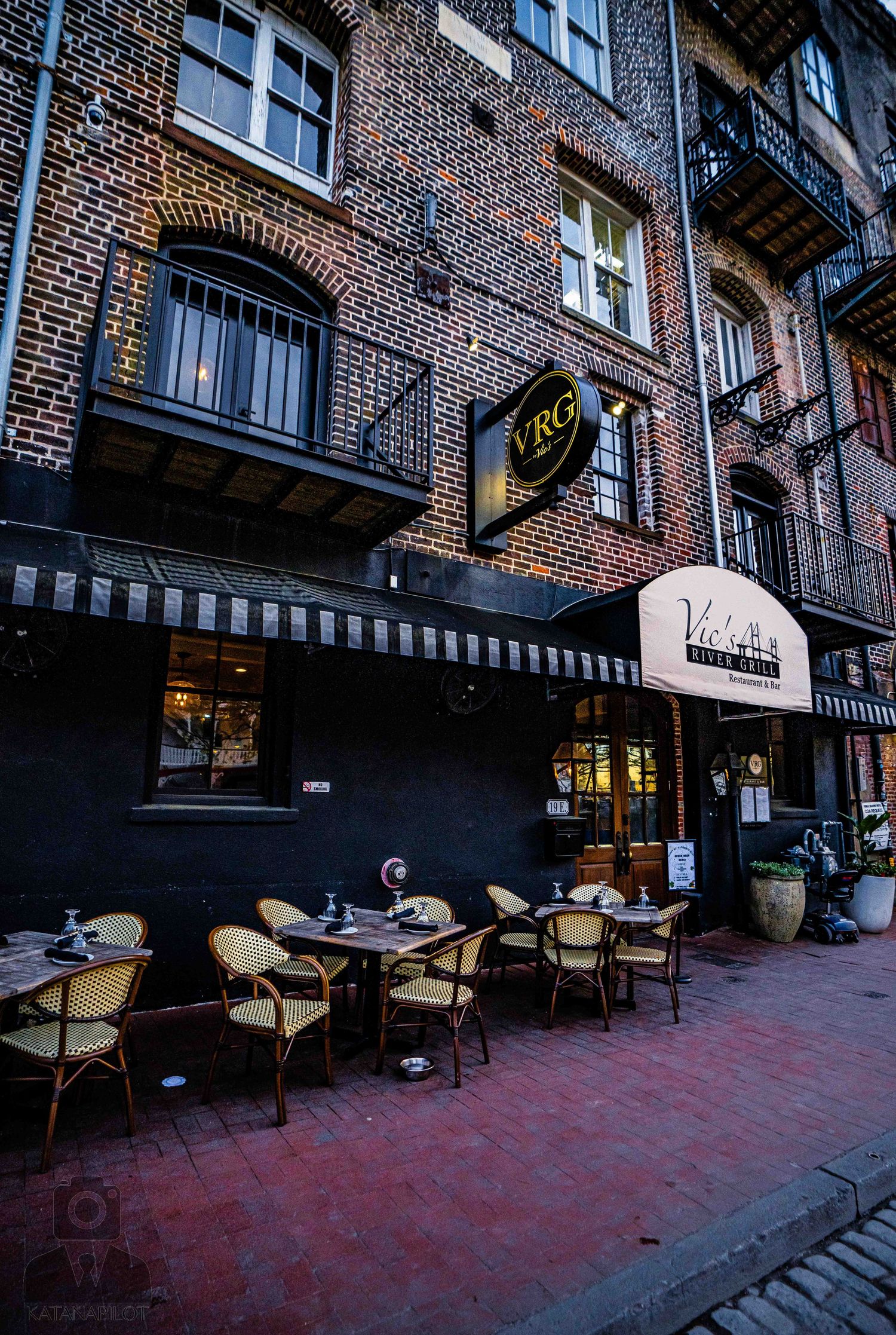 Historic brick building facade with outdoor cafe seating and red brick sidewalk in an urban setting.