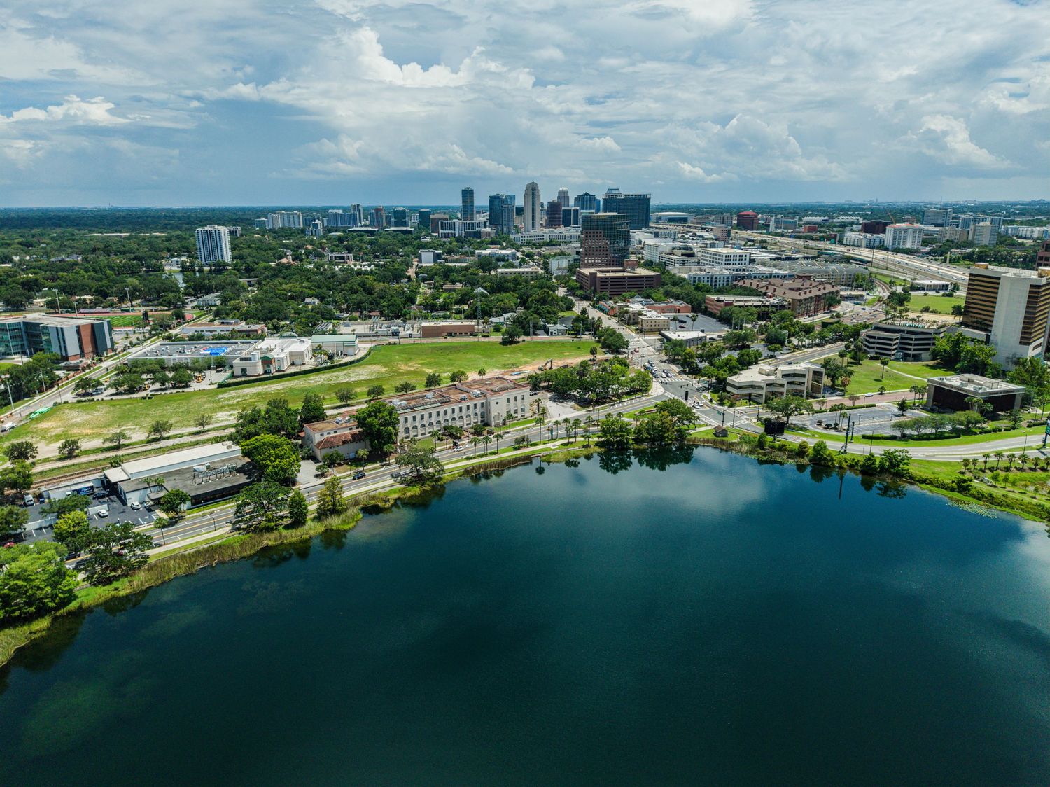 Aerial view of Orlando Florida skyline with lush green trees and a serene blue lake in the foreground.