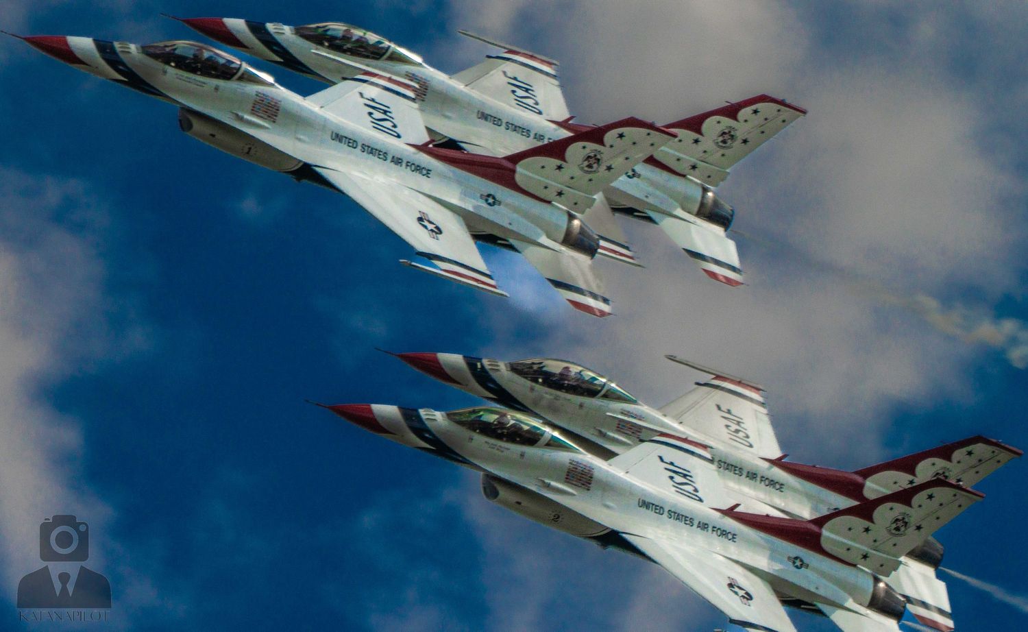 Four US Air Force Thunderbirds F-16 jets fly in tight formation against a dramatic cloudy blue sky.
