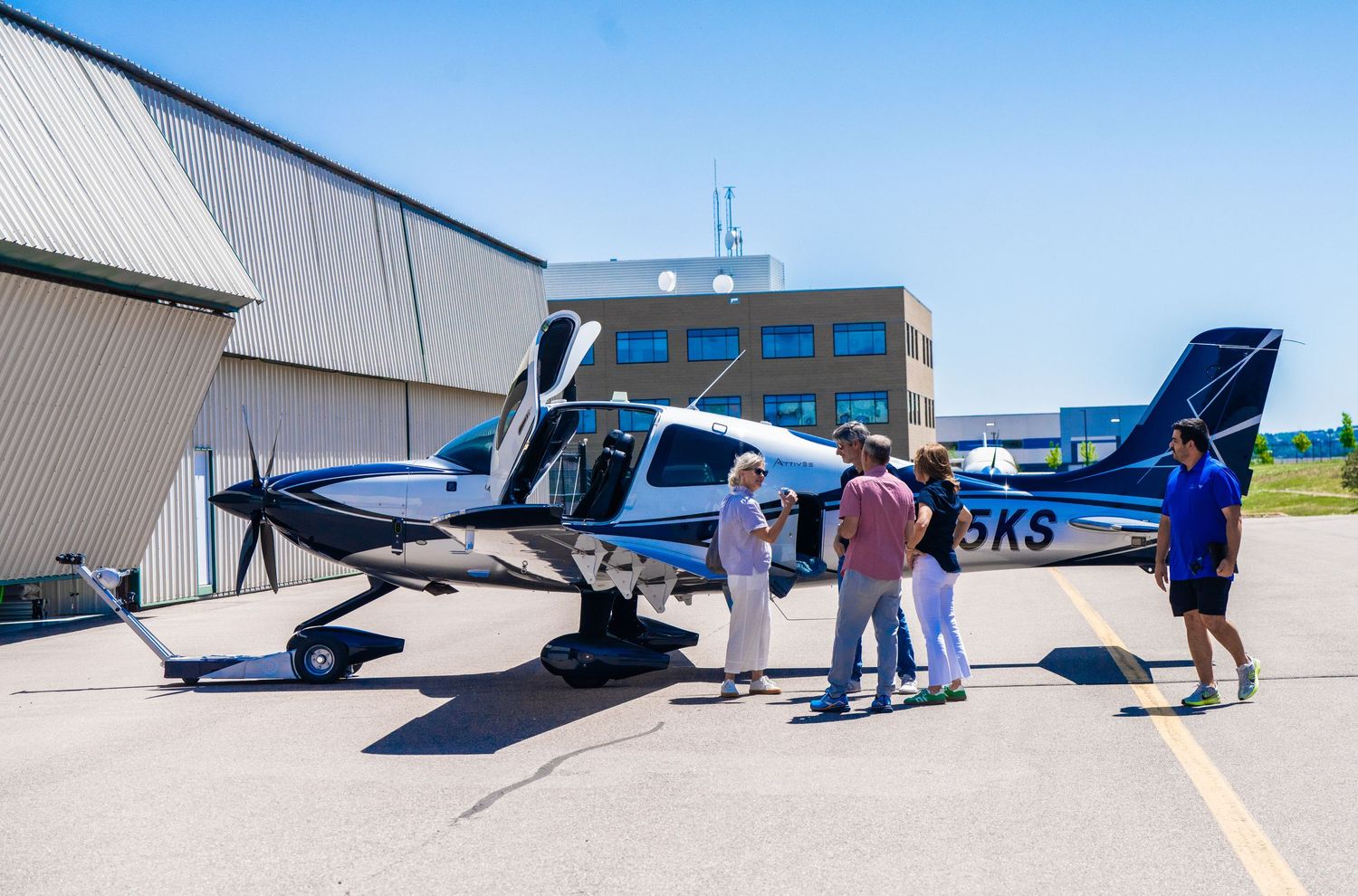 Multiple small aircraft lined up on airport tarmac with people inspecting them.