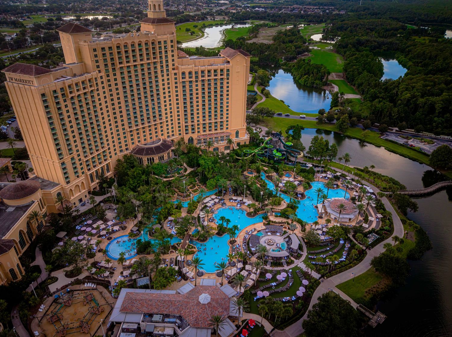 Aerial view of a luxury resort hotel with a large pool complex, lush landscaping, and a scenic lake in Orlando, Florida.