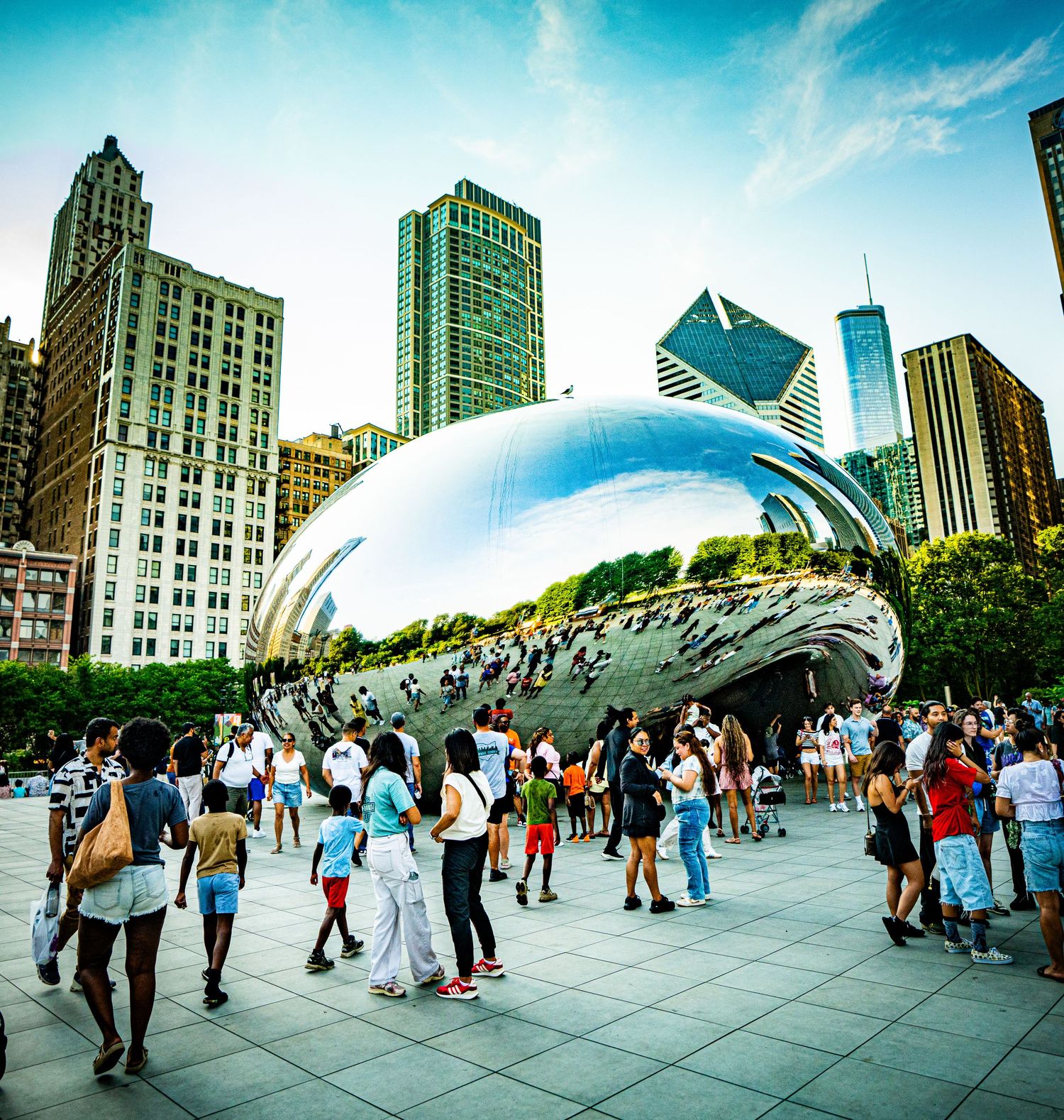 Crowds gather around the iconic Cloud Gate sculpture in Chicago's Millennium Park with city skyline in background.